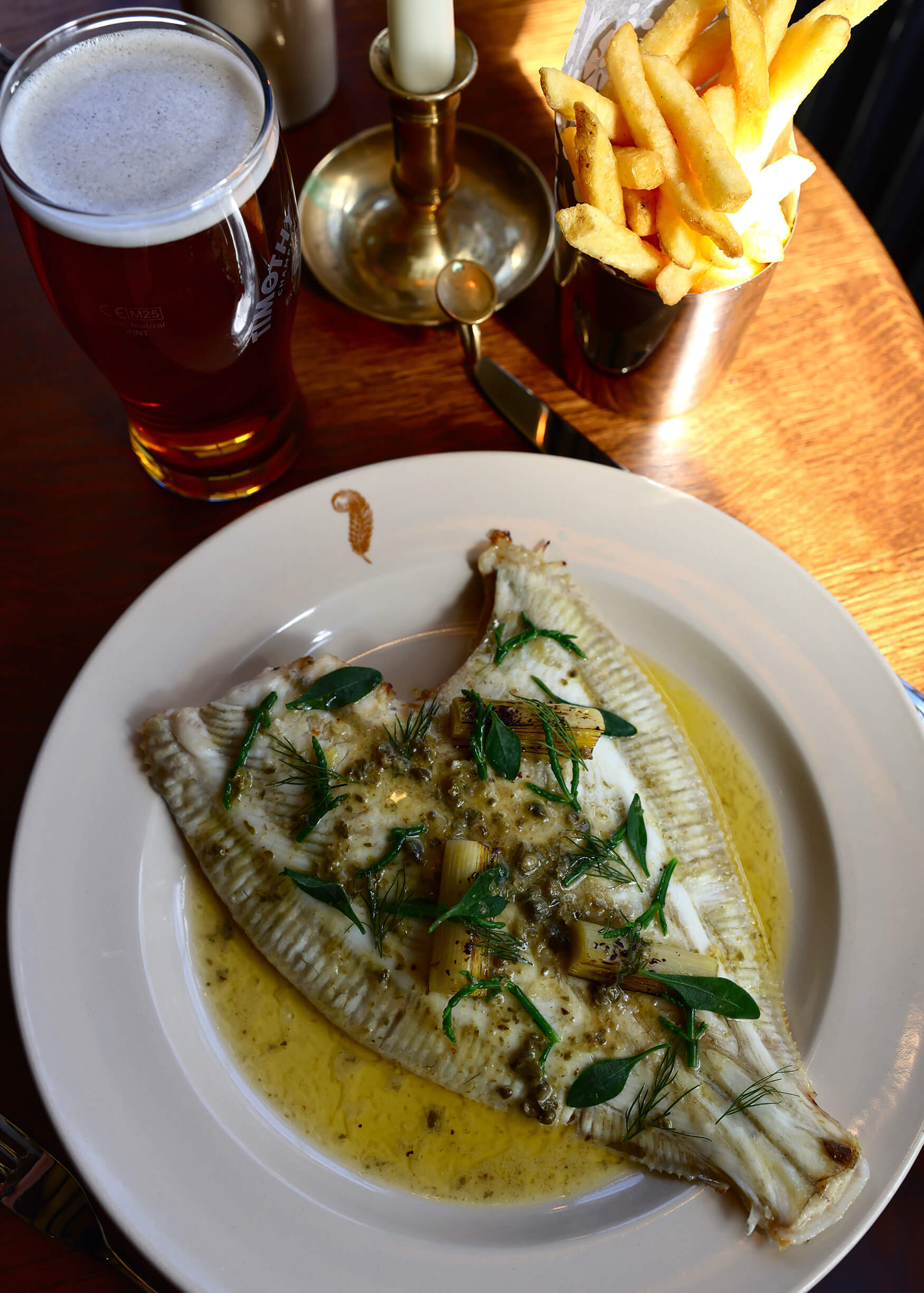 Overhead shot of a white fish covered in melted butter with chips and a beer at The General Tarleton