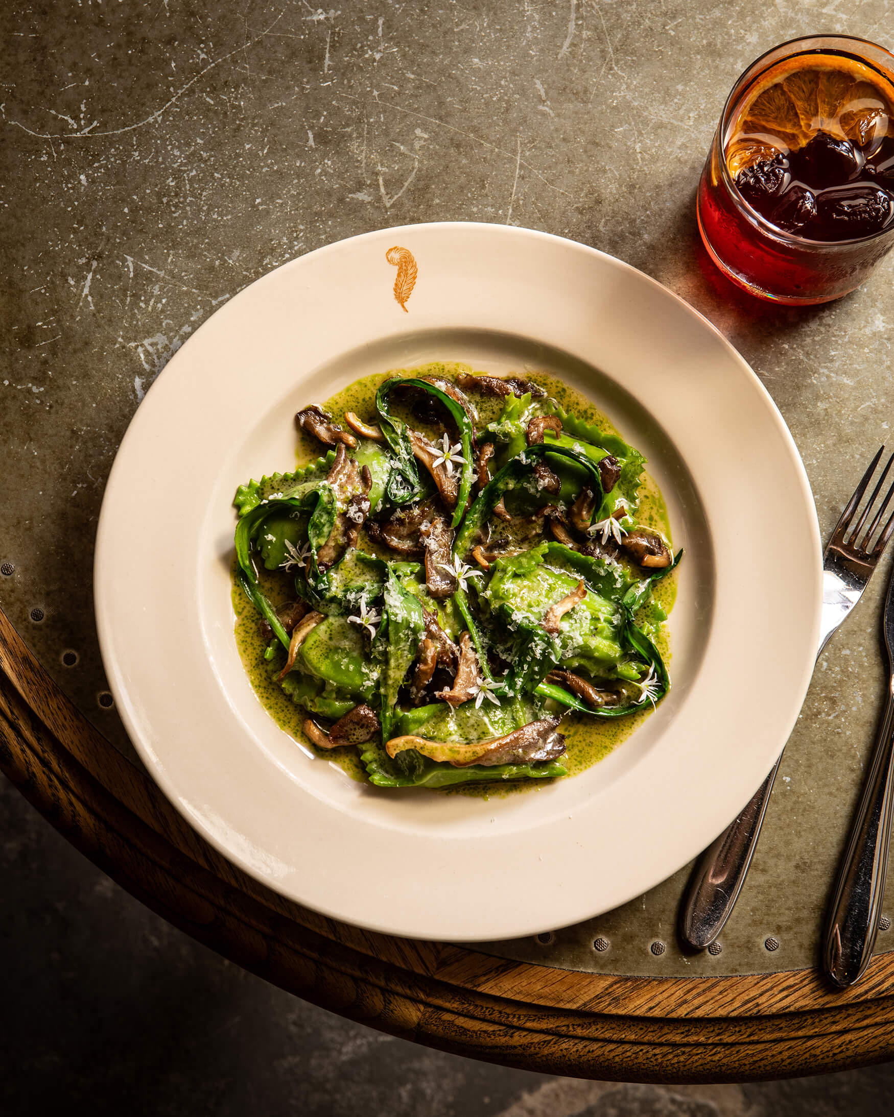 Overhead shot of a wild mushroom pasta sitting on a pewter table with a negroni at The General Tarleton