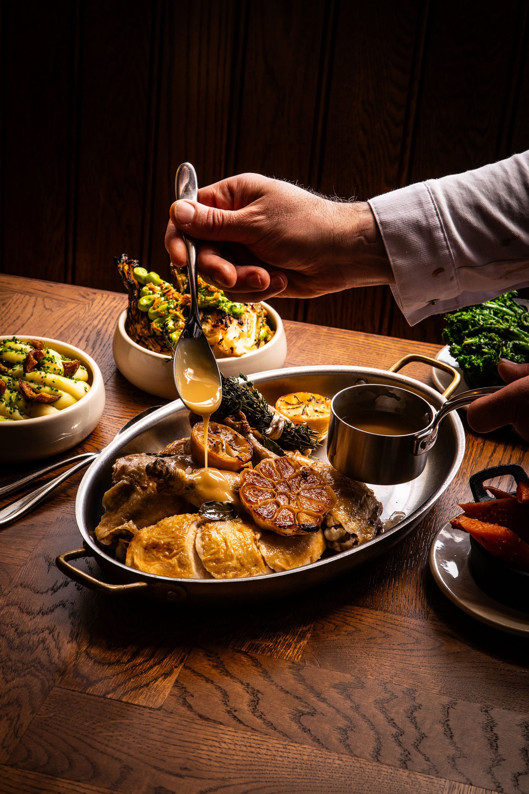 Sharing chicken dish with all the trimmings sitting on a wooden table with a hand reaching in to pour jus over the chicken at The General Tarleton