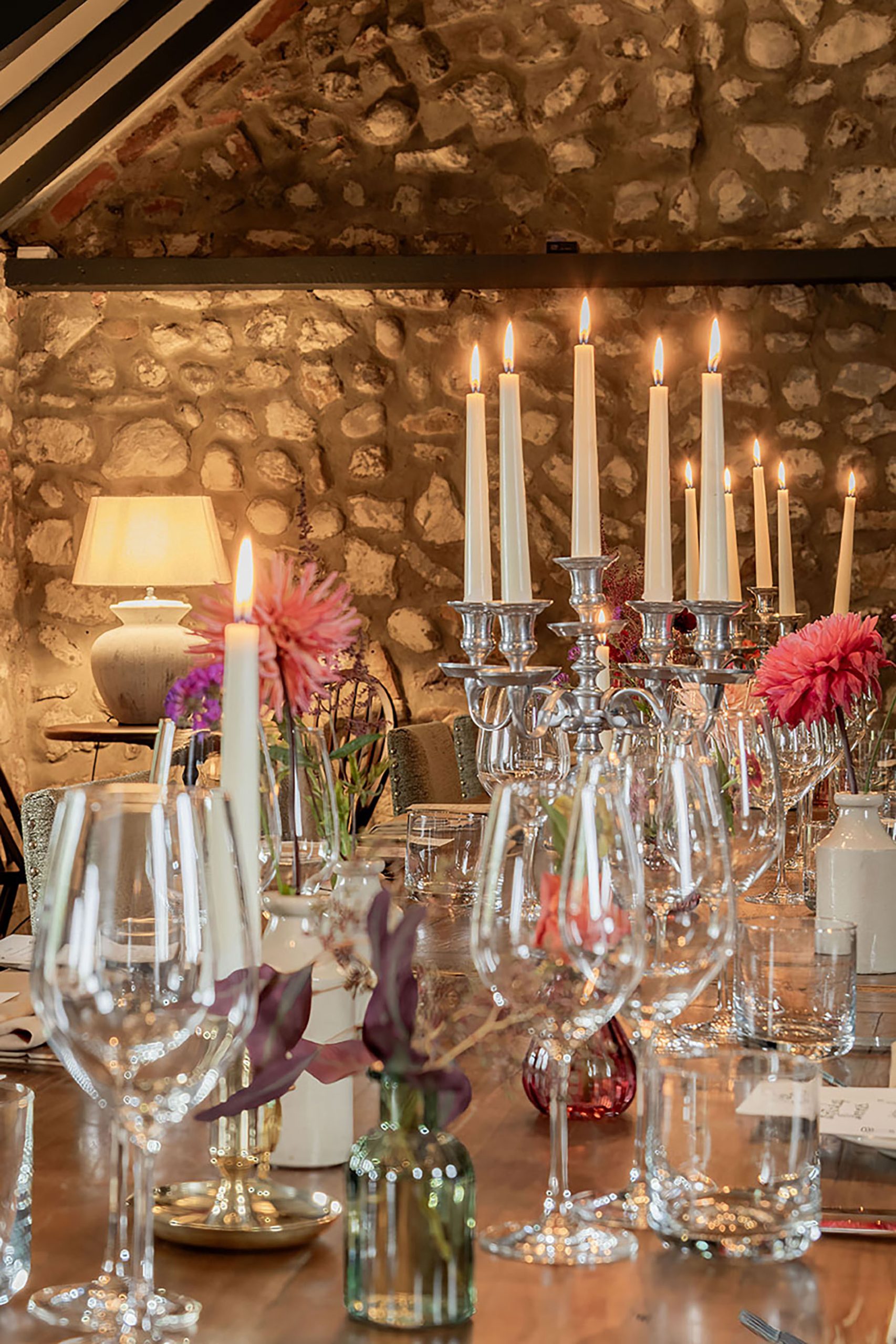 Image of a beautiful stone walled room with wooden beams, in which a table is lain with candles lit for a large private party at The General Tarleton