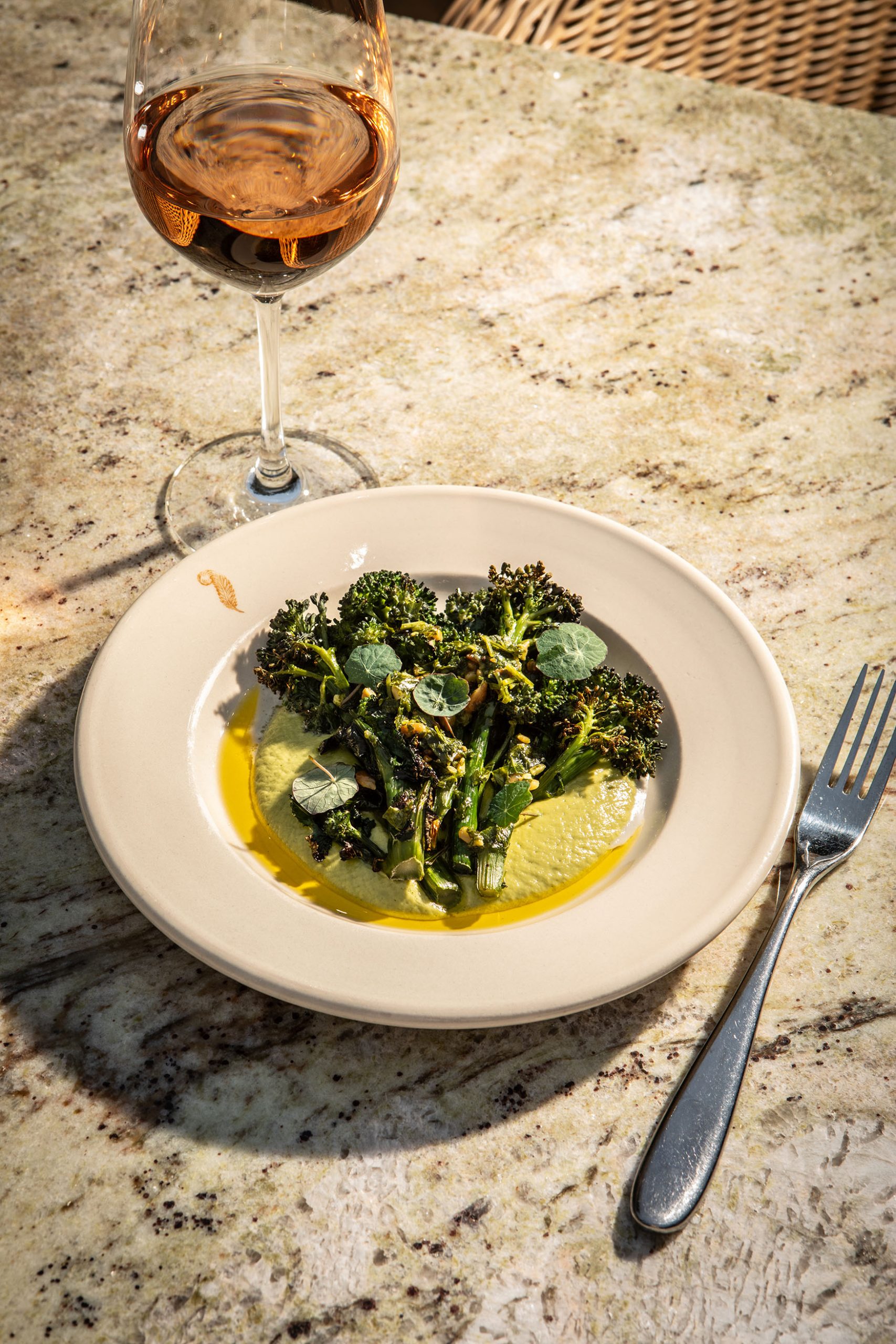 Image of a side plate of broccoli and a glass of Rosé on a marble table on The Terrace at The General Tarleton